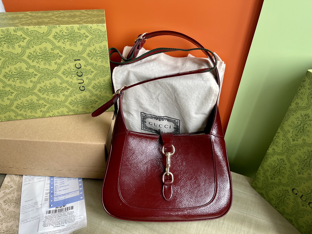 Nº de modelo: 782849 Talla: 27,5/19/4 P1760 Este nuevo bolso bandolera Gucci Jackie está confeccionado con pieles de la mejor calidad y muestra la artesanía, la forma de media luna y el elegante diseño del icónico bolso bandolera de la marca. La combinación de herrajes en tono dorado claro, ribetes de piel y una correa de cortesía ribeteada con cincha roja y verde aporta aún más posibilidades de estilo a este bolso bandolera pequeño Gucci Jackie en charol rojo. La combinación de ribetes de piel y una correa adicional ribeteada con cincha roja y verde aporta aún más posibilidades de estilo a este bolso bandolera pequeño Gucci Jackie, confeccionado en charol rojo.Charol rojoHerrajes en tono dorado claroForro de pielInterior: un bolsillo con cremallera con escudo GucciAsas con cremallera (18 cm de altura)Correa bandolera de cincha extraíble (52 cm de altura)Cierre de gancho y lazo-Fábrica de alto impacto