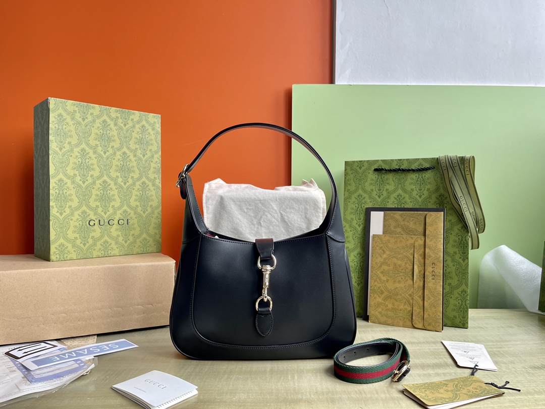 Modelo: 782849 Tamanho: 27.5/19/4 P1900 Esta nova bolsa de ombro Gucci Jackie é confeccionada com couros da melhor qualidade e mostra a habilidade artesanal, a forma crescente e o design elegante das icônicas bolsas de ombro da marca. A combinação de ferragens douradas, debrum de couro e alças listradas adicionais traz mais possibilidades de uso para a bolsa de ombro Gucci Jackie, que vem em um pequeno couro sintético preto. A combinação de pele preta, ferragens em tom dourado claro, debrum em pele e alças adicionais às riscas confere ainda mais versatilidade a esta pequena mala de ombro da coleção Gucci Jackie.Pele pretaCouro em tom dourado claroRevestimento em peleInterior: um bolso com fecho de correr com emblema GucciPuxadores com fecho de correr (18 cm de altura)Alça de ombro amovível em tecido (52 cm de altura)Fecho com gancho e argolaFábricas de alto impacto