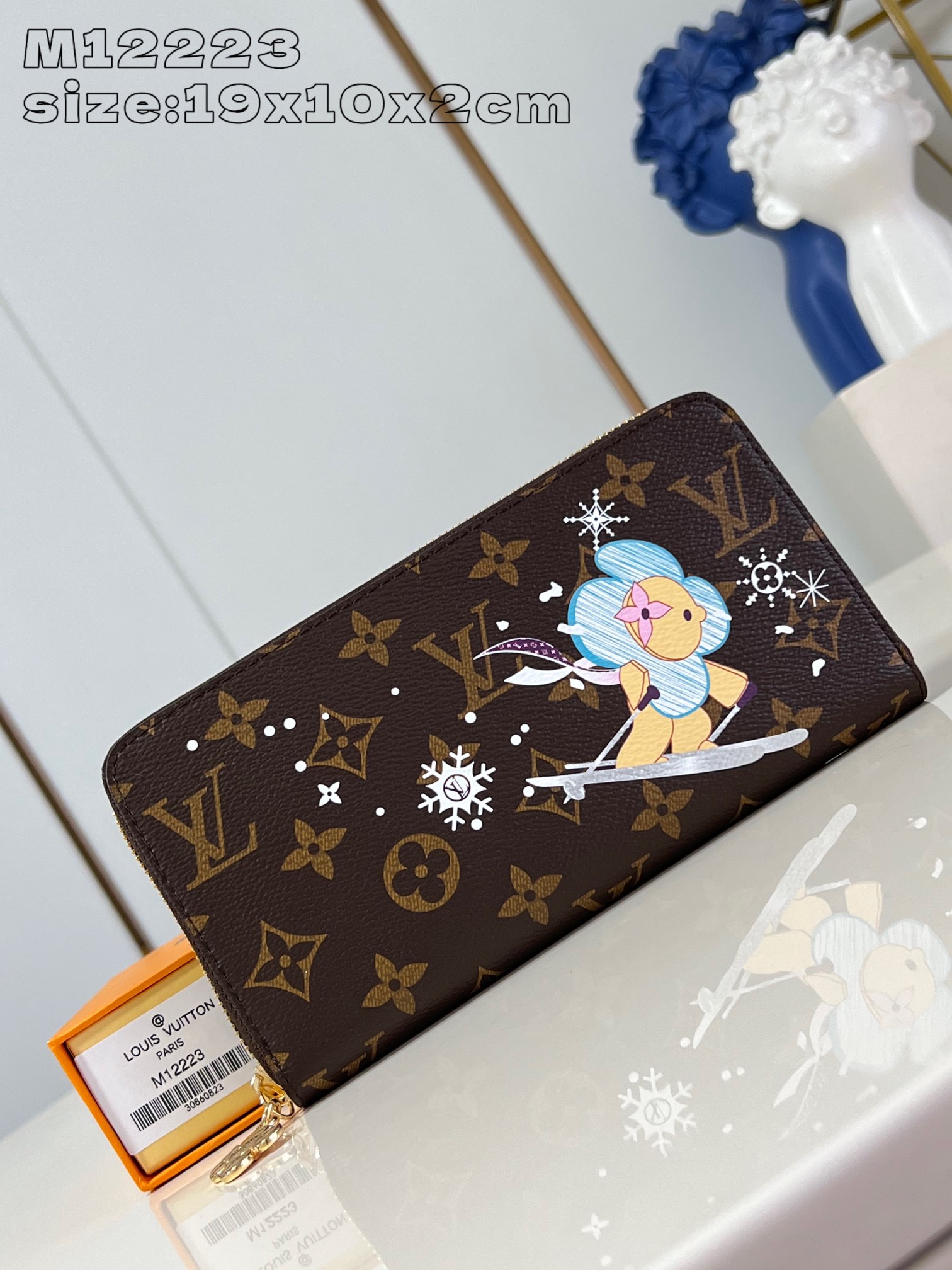 M12223 This festive zippy wallet from the Snow Show collection features Louis Vuitton's Vivienne mascot skiing in the LV snowflakes. Crafted in the iconic Monogram canvas and lined in Azur Frost leather, this playful design comes with multiple interior pockets, three compartments, and twelve business card slots 19.5 x 10.5 cm (L x H x W). x 2.5 cm (L x H x W)