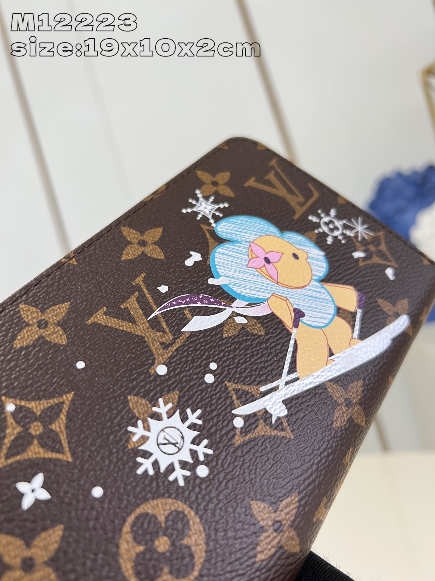 M12223 This festive zippy wallet from the Snow Show collection features Louis Vuitton's Vivienne mascot skiing in the LV snowflakes. Crafted in the iconic Monogram canvas and lined in Azur Frost leather, this playful design comes with multiple interior pockets, three compartments, and twelve business card slots 19.5 x 10.5 cm (L x H x W). x 2.5 cm (L x H x W)