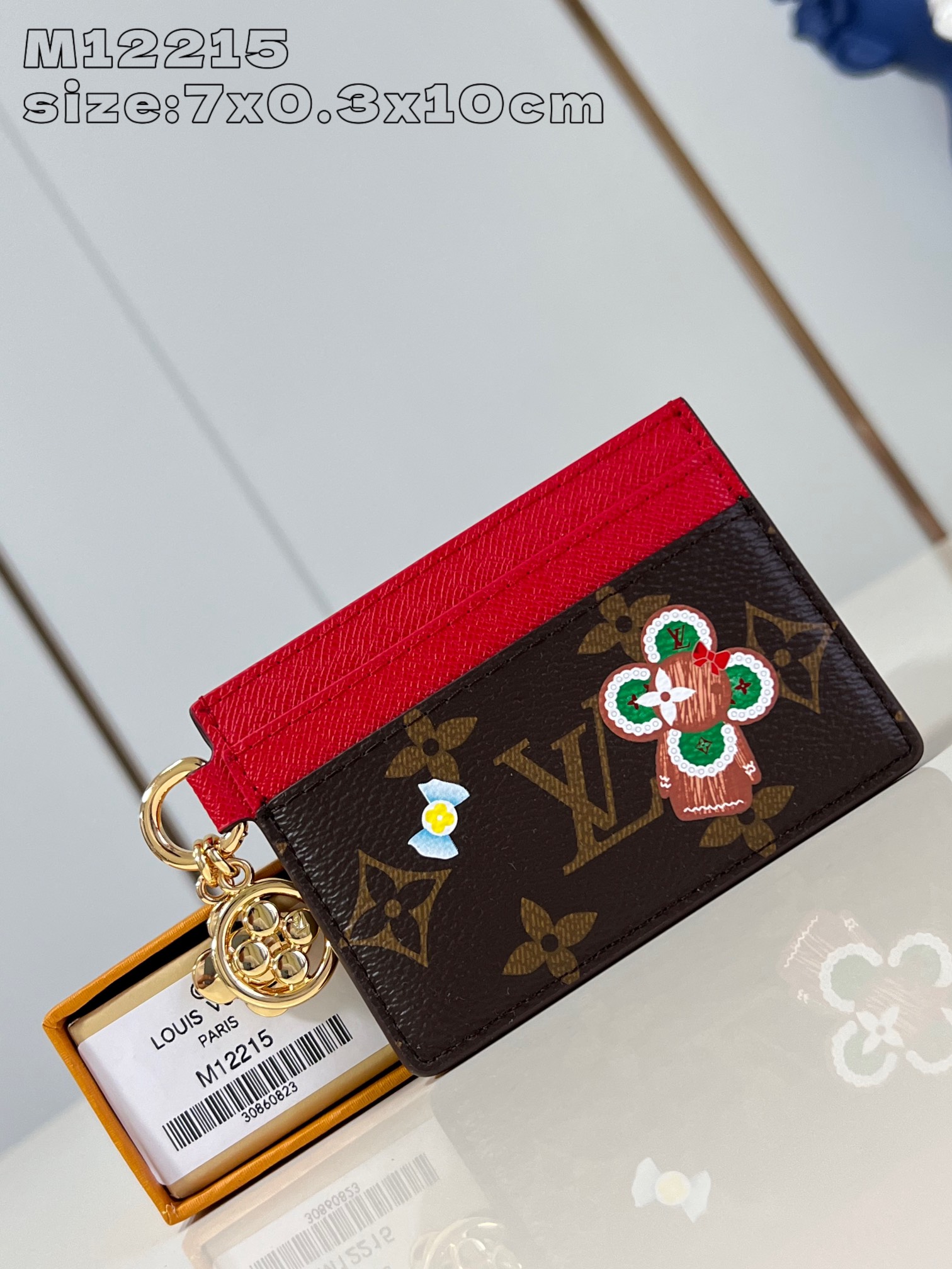 M12215 This LV Charms card holder from the Candy Factory collection invites the brand's mascot to celebrate the holiday season with a Monogram canvas depicting Vivienne wandering through a joyful landscape of candy Vivienne stylized embellishments and LV floral detailing 7.3 x 0.3 x 10.2 cm (H x W x L).