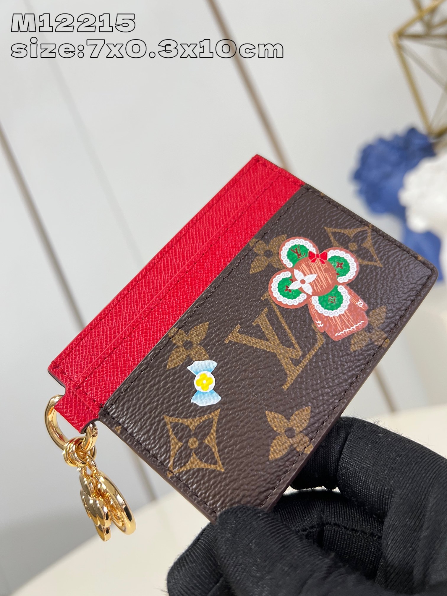 M12215 This LV Charms card holder from the Candy Factory collection invites the brand's mascot to celebrate the holiday season with a Monogram canvas depicting Vivienne wandering through a joyful landscape of candy Vivienne stylized embellishments and LV floral detailing 7.3 x 0.3 x 10.2 cm (H x W x L).