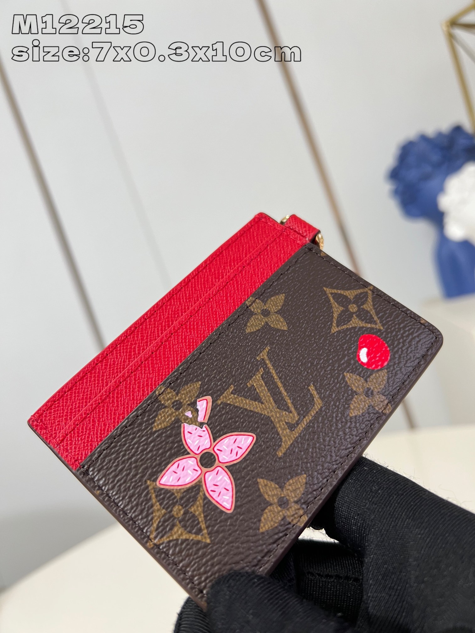 M12215 This LV Charms card holder from the Candy Factory collection invites the brand's mascot to celebrate the holiday season with a Monogram canvas depicting Vivienne wandering through a joyful landscape of candy Vivienne stylized embellishments and LV floral detailing 7.3 x 0.3 x 10.2 cm (H x W x L).