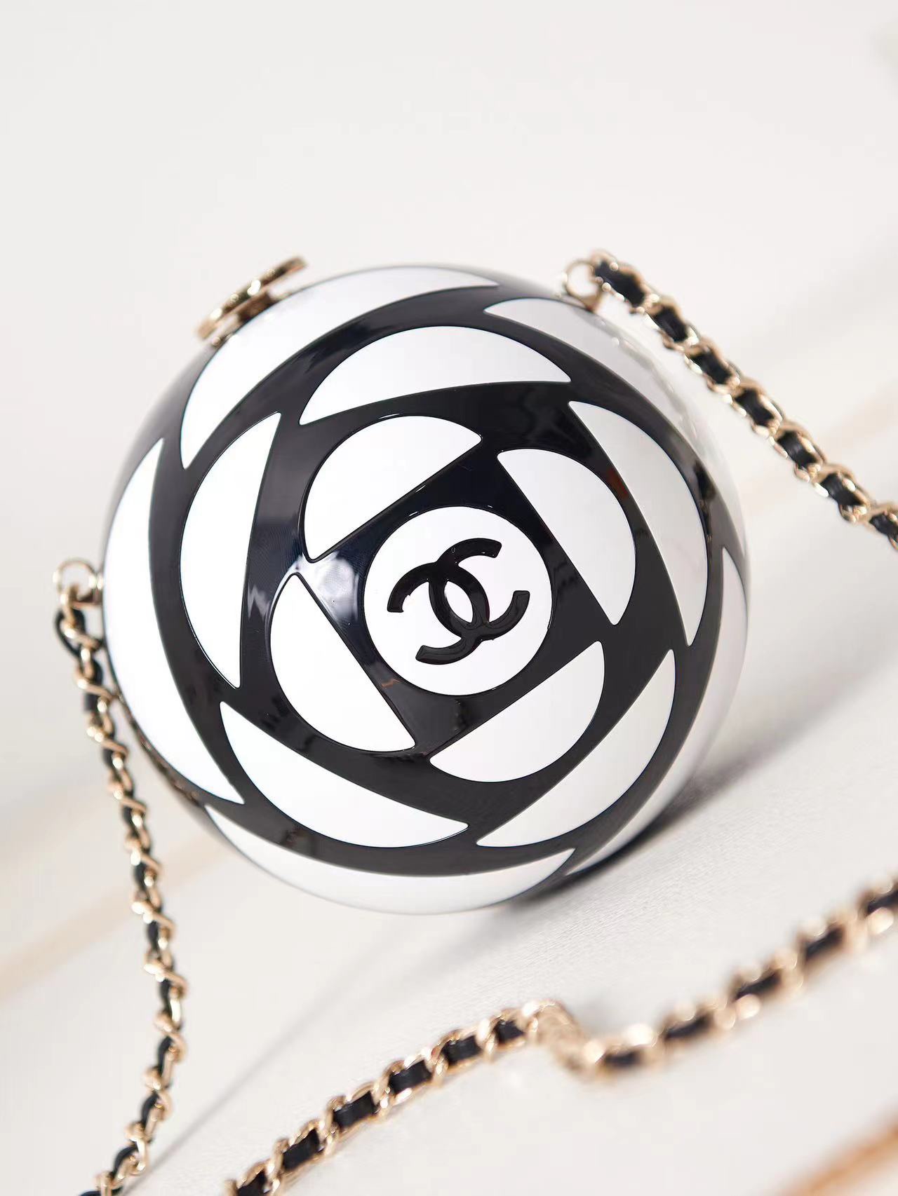 CHANEL 2023K Camellia In stockThe spring/summer fashion week saw the launch of a spherical evening bag.Its black and white color scheme is almost identical to that of a soccer ball.The ball-shaped evening bagResin, enamel and gold leather chain. Metallic black and whiteHeavily crafted.Model No. AS3716Size 12-12-12