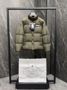 P1320 プレミアムダウン ⬆️Prada リナイロン リサイクルナイロンダウンジャケット。2024ニュージャカードライニング。スーパーフルパディング。プレミアムグースダウンパディング ➕オリジナルハードウェア。完全組み立て式。スーツバッグ、ハンガー、ショッピングバッグ付き。ギフトボックス入り。モダンなシルエットのダウンジャケットは、スポーティなスタイルと洗練されたディテールが融合。カジュアルなデザインにエナメル加工を施した三角形のメタルロゴをあしらい、中わた入りの襟とグースダウンを使用。-オーバーサイズフィット-ふっくらとした襟-ストレートスリーブ-袖口はスナップボタンで調節可能。-ジッパー開閉式-ポケット付き-ストレートカフス-肩幅-裾はフラット-レザートリム-グースダウンの裏地と中わた-胸にエナメル加工を施した三角形のメタルロゴ。サイズ：48-56 ブラック・グリーン