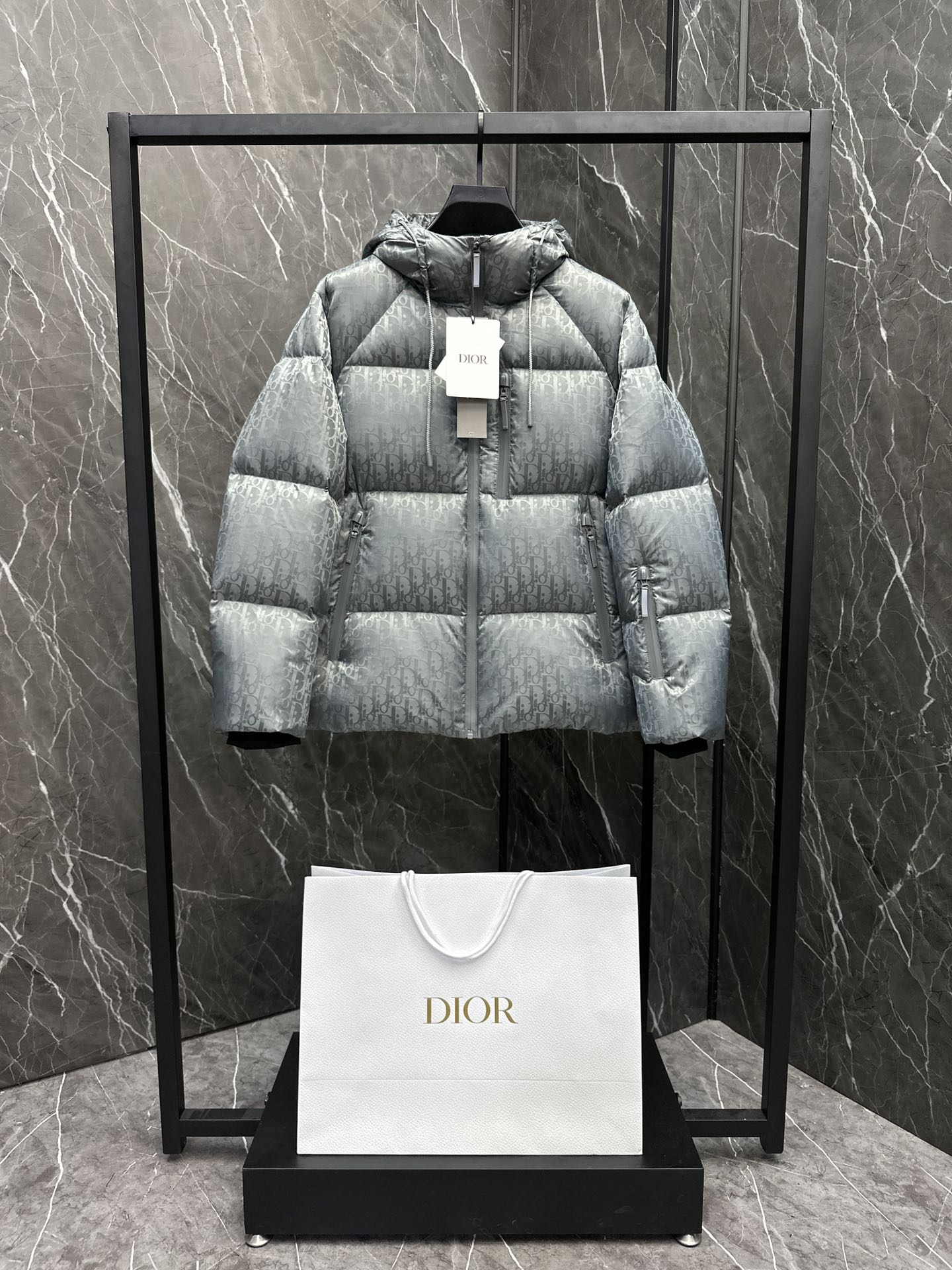 P1360 Dior CD Dior tech fabric Doudoune à capuche imprimée en oblique. Rembourrage en duvet d'oie. Très ample. Une seule pièce pour l'hiver. Cette doudoune est réalisée en jacquard techno avec un imprimé Oblique ton sur ton qui rend hommage à l'héritage de Dior. Décontractée mais élégante, elle est dotée d'une fermeture à glissière de compression coupe-vent et d'un rembourrage en duvet d'oie chaud qui ajoutera une touche classique à n'importe quel look -Imprimé Oblique ton sur ton sur le corps -Capuchon Fermeture à glissière de compression coupe-vent. Fermeture à glissière gravée du logo Dior - Poches latérales plaquées et poches intérieures - Rembourrage : 90% de duvet d'oie blanc 10% de plumes d'oie blanche - Matière : 100% nylon, sauf pour les garnitures - Matière 2 100% nylon, broderie - 50% nylon. 50% PVC Matière 3 100% Polyester-Fabriqué en ItalieTaille : 48-56 noir/gris-Sacs haute couture