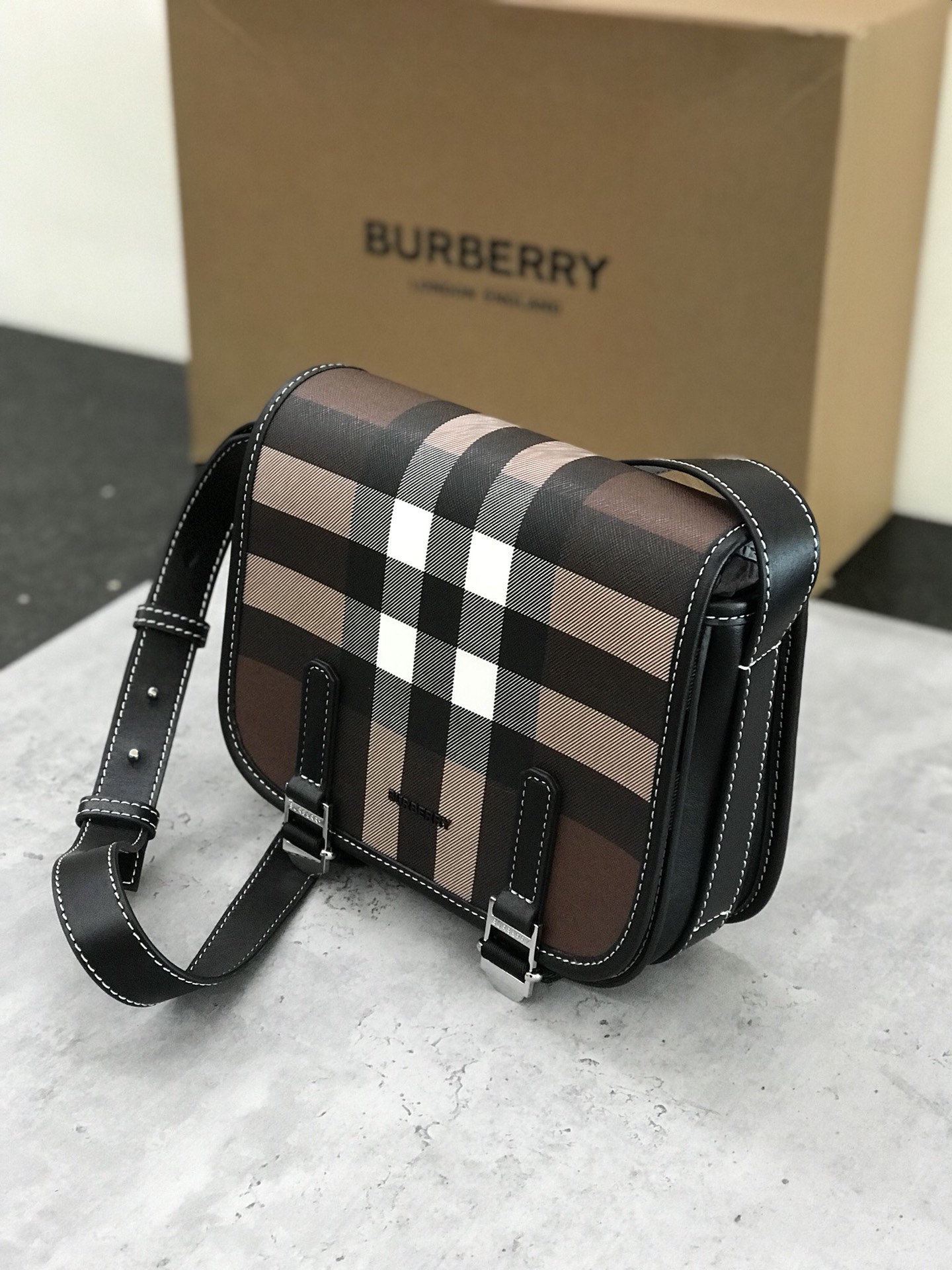 Burberry's sleek messenger bag is updated in checkered eco-canvas, which is made from renewable resources and requires less water and generates less carbon dioxide than traditional coated canvas. The bag is printed with a logo and trimmed with a striped leather trim and an adjustable shoulder strap. 1 external pocket with hidden magnetic closure; 1 internal zipped pocket; 1 internal slit pocket. Fold-over front flap with snap and buckle closure. Hand-painted edges. Shiny metal hardware. Burberry monogrammed logo on front.22x19x7 p900