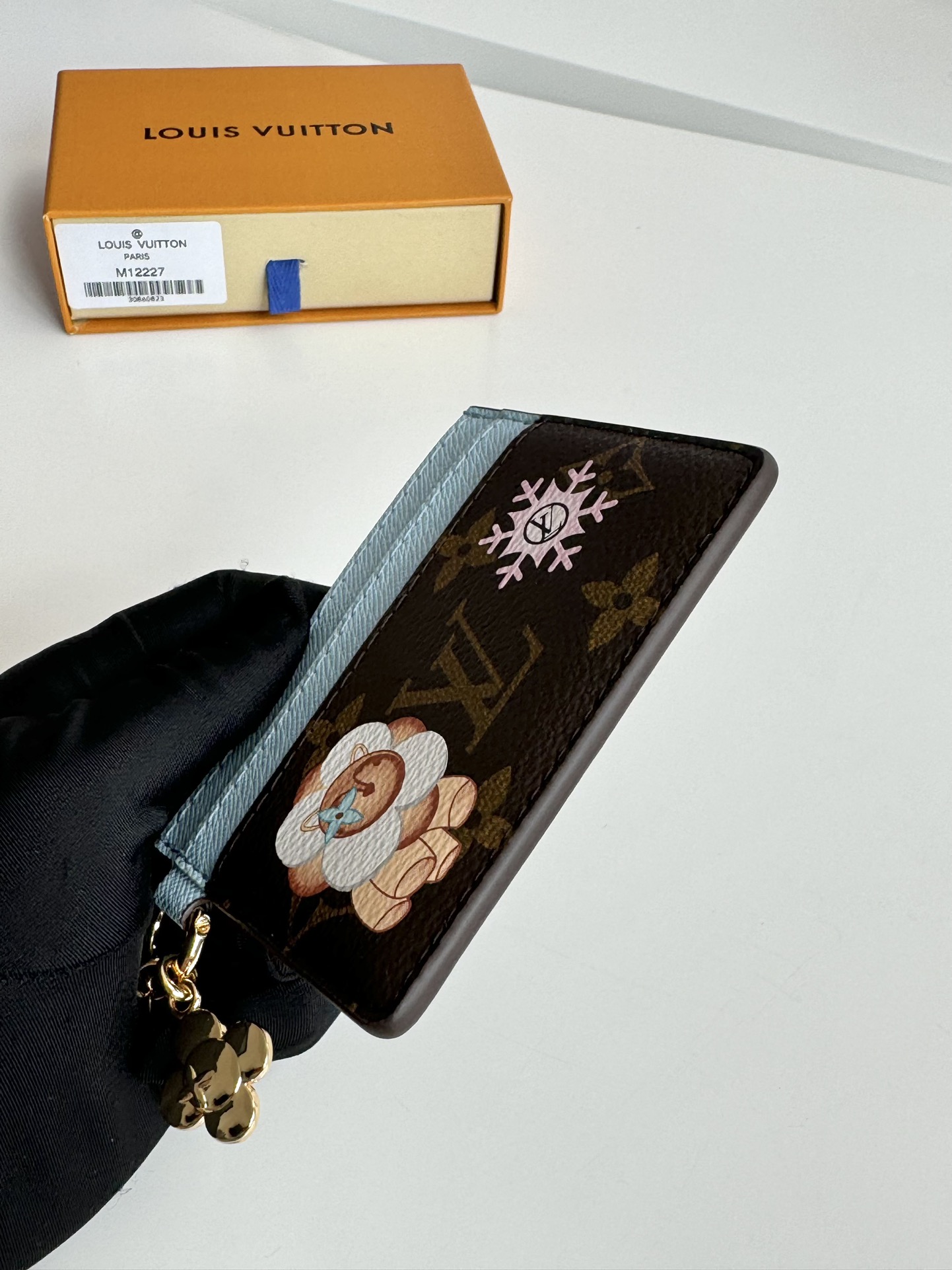 P320 M12215 This LV Charms card holder from the Candy Factory collection invites the brand's mascot to celebrate the holiday season Monclerogram canvas depicts Vivienne wandering through a joyful landscape of colorful candies Vivienne styling embellishments and LV floral detailing Dimensions: 10 x 7.3cm.