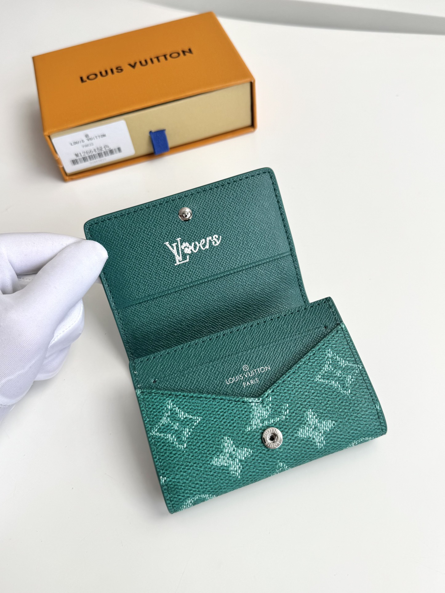 P320 M12664 Green This business card holder in Monclerogram Heritage canvas has a slim silhouette and can be easily slipped into a pocket or handbag flap. It opens with a hidden snap closure that reveals an organza compartment and card slots. Cowhide leather lining and the Marque L.Vuitton Déposée logo in Damier canvas add sophisticated detailing to the size: 10.5 x 8 x 1cm