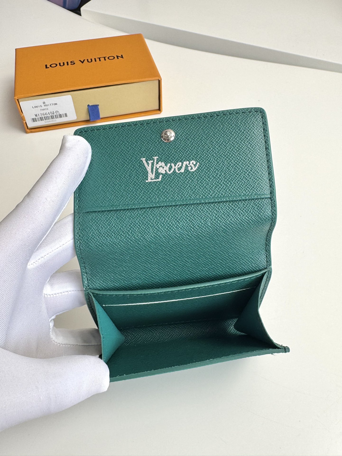 P320 M12664 Verde Este tarjetero en lona Monclerogram Heritage tiene una silueta estilizada y puede deslizarse fácilmente en un bolsillo o en la solapa de un bolso de mano. Se abre con un cierre a presión oculto que revela un compartimento de organza y ranuras para tarjetas. El forro de piel de vaca y el logotipo Marque L'Vuitton Déposée sobre lona Damier añaden detalles sofisticados a sus dimensiones: 10,5 x 8 x 1 cm