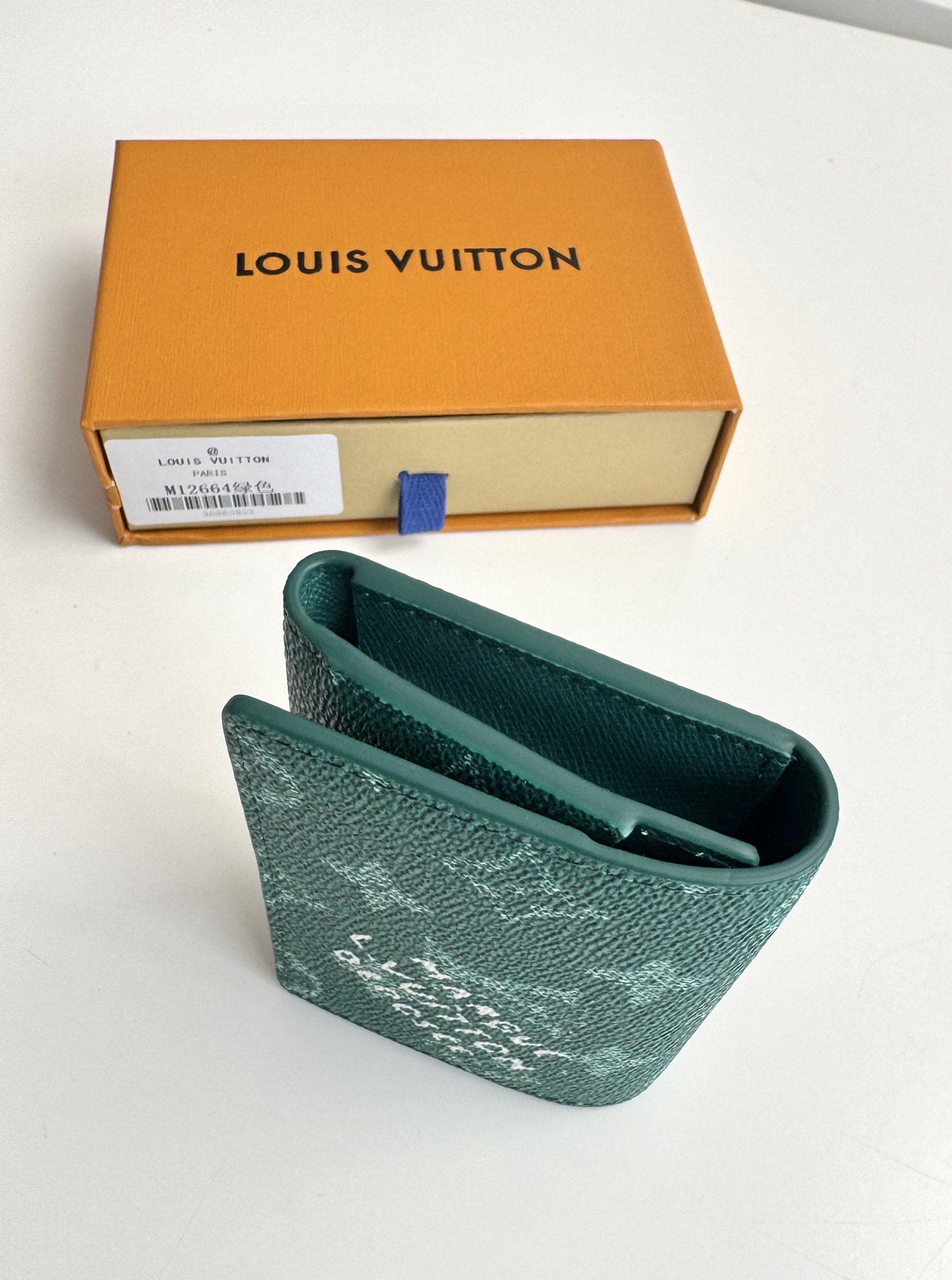 P320 M12664 Green This business card holder in Monclerogram Heritage canvas has a slim silhouette and can be easily slipped into a pocket or handbag flap. It opens with a hidden snap closure that reveals an organza compartment and card slots. Cowhide leather lining and the Marque L.Vuitton Déposée logo in Damier canvas add sophisticated detailing to the size: 10.5 x 8 x 1cm