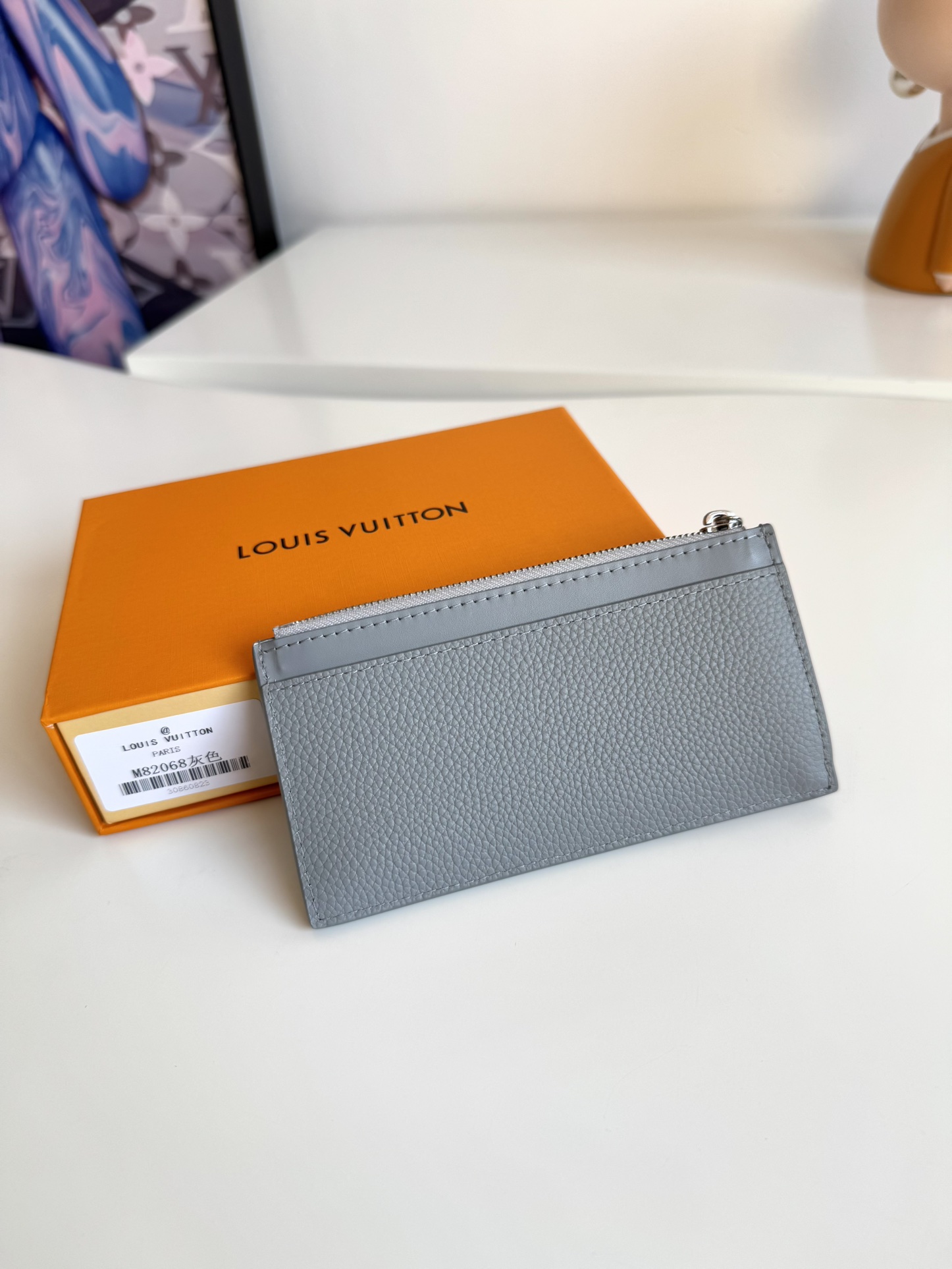 P360 M82068 Gray Tailored from Louis Vuitton's iconic Taiga leather, the Coin Card Holder has a sleek, clean look and is ideal for securely storing loose change and banknotes. Inside, there are multiple credit card slots and bill compartments, plus an additional zippered coin pocket.