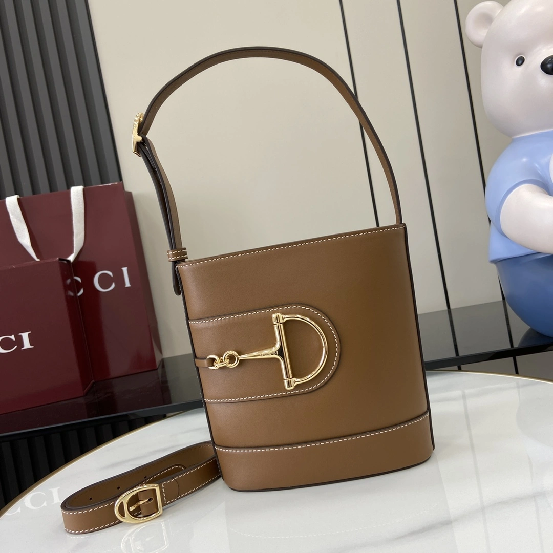 p1080 Para la colección Primavera/Verano 2025, Gucci 73 se inspira en un bolso cubo de colección lanzado el mismo año que su homónimo Este bolso es una interpretación estética moderna del accesorio con forma de bocado que puede llevarse cruzado, colgado del hombro o como bolso de mano Piel marrón brillante Tono dorado Accesorio de gran tamaño con forma de medio bocado Forro en mezcla de algodón y lino marrón Interior: 1 bolsillo con cremallera Correa para el hombro (19 cm de altura); Cierre con hebilla magnética Modelo: 833665 Medidas: 18,5 cm (ancho) x 20 cm (alto) x 8,5 cm (fondo) Color: Marrón Piel/peso: aprox. 0,5 kg Italian Creations-High Fidelity Bags