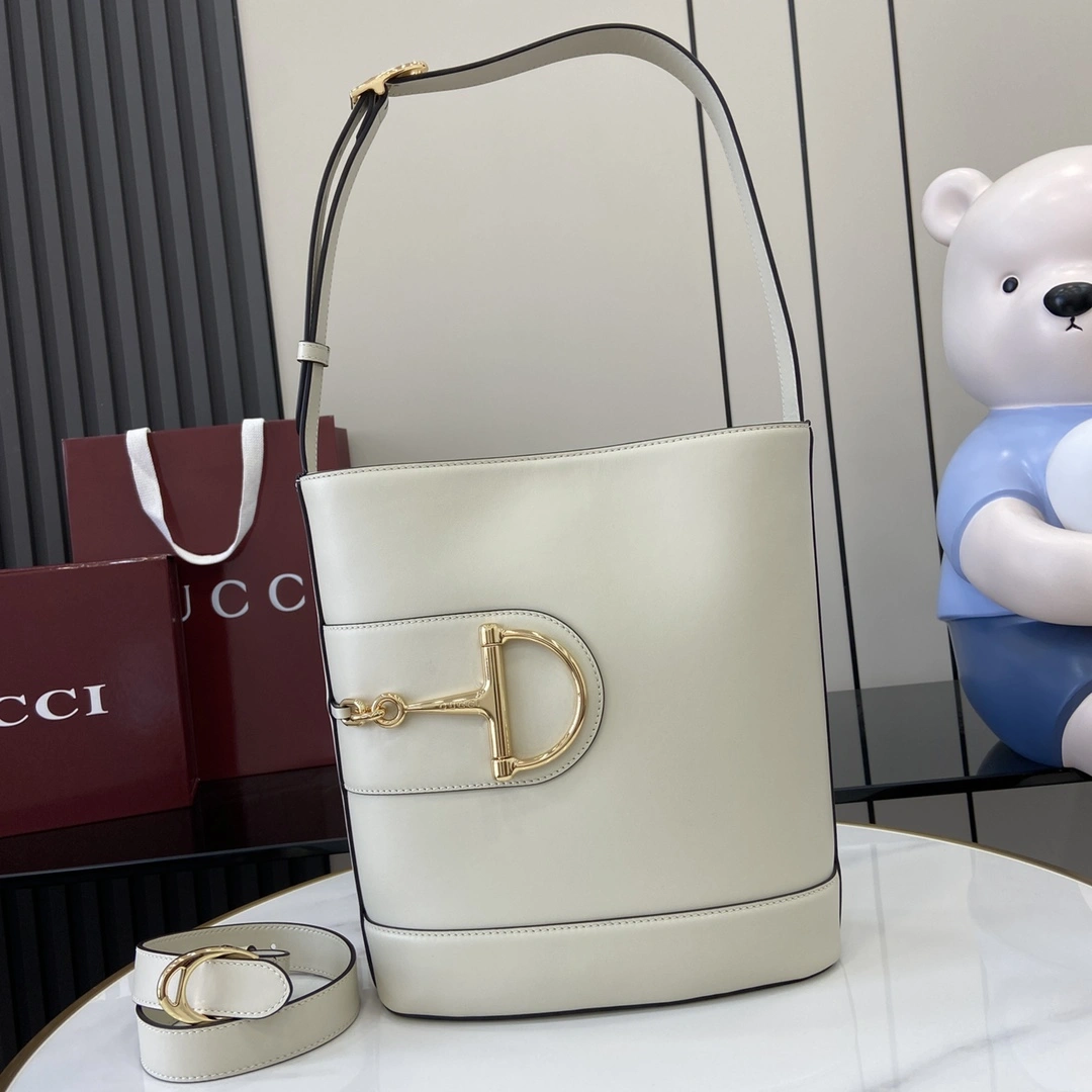 p1380 For the Spring/Summer 2025 collection Gucci 73 takes inspiration from a collectible bucket bag launched the same year as its namesake This bag is a modern aesthetic interpretation of the horsebit shape accessory It can be worn crossbody, over the shoulder or as a handbag White glossy leather Gold tone Oversized half horsebit shape accessory Brown cotton and linen blend lining Interior: 1 zipper pouch Shoulder strap (27 cm high); Comes with detachable bag (50 cm high) Magnetic snap closure Model: 833660 Size: 26 cm (W) x 27.5 cm (H) x 11.5 cm (D) Color: White Full Leather/Weight: Approx. 0.8 kg Italian Creations - High-quality Bags